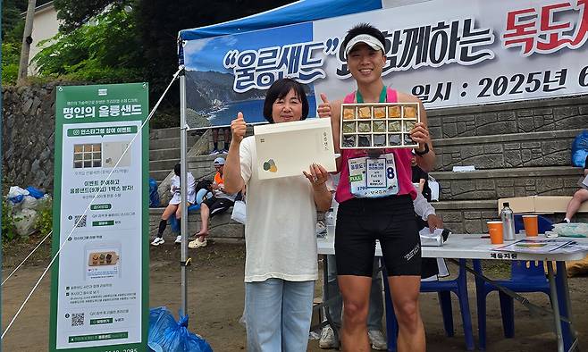 지난 15일 울릉군 울릉읍 사동리 울릉문화예술체험관 일원에서 열린 '제20회 울릉 국제마라톤대회' 행사장에서 최기정(왼쪽) 브래드필 대표와 마라톤 풀코스 우승자 안은태(오른쪽)씨가 울릉샌드 제품을 들고 기념촬영을 하고 있다.&nbsp;