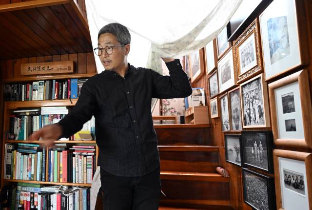 노순택 사진가가 자택에서 잠시 커튼을 들어 올리며 정리 중인 사진과 책이 있는 일부 공간을 보여주고 있다.