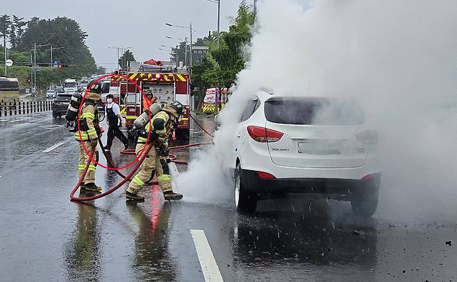 지난 16일 제주시내 도로에서 차량에 불이 나자 인근 카페 직원들과 소방관들이 불을 끄고 있다./제주도소방안전본부