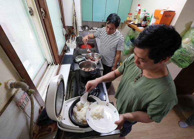 Sokkoko Han, left, a foreign worker employed by a subcontractor at a major shipyard in Geoje, South Gyeongsang, and his colleague boil a chunk of pig’s trotter and cook rice for dinner in their two-room apartment on June 5. [JOONGANG ILBO]