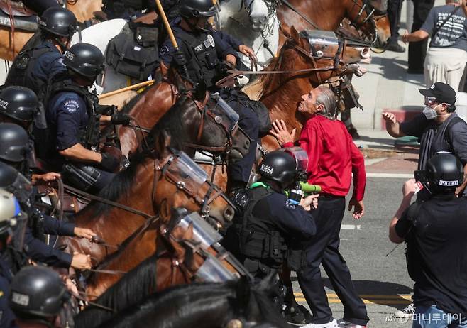 14일(현지시간) 미국 캘리포니아주 로스앤젤레스(LA)에서 도널드 트럼프 미국 대통령의 정책과 연방 이민 단속에 반대하는 '노 킹스'(No Kings) 시위에서 한 시위 참여자가 기마 경찰을 막고 있다. 2/로이터=뉴스1