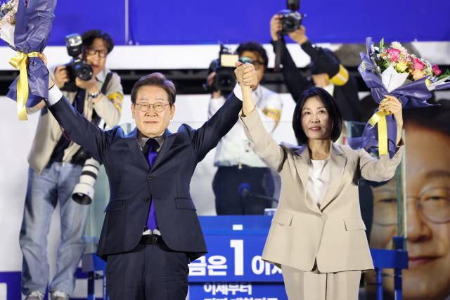 ▲제21대 대통령 당선이 확실시되는 더불어민주당 이재명 대선 후보와 부인 김혜경 여사가 4일 서울 여의도 국회 인근에서 당 주최로 열린 국민개표방송 행사에 참석해 꽃다발을 받고서 시민들을 향해 두 팔을 들어올려 인사하고 있다. ⓒ연합뉴스