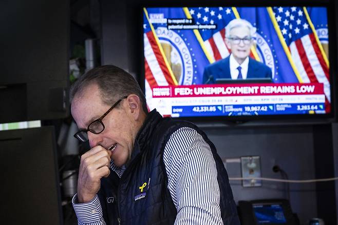 18일(현지시간) 미국 뉴욕증권거래소(NYSE)에서 한 트레이더가 제롬 파월 미 연방준비제도(Fed·연준) 의장의 기자회견 모습이 담긴 TV 화면 밑에서 주식 거래에 집중하고 있다. [EPA]