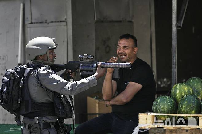 [나블루스=AP/뉴시스]지난 5월 21일 요르단강 서안지구 나블루스 인근 아스카르 난민캠프에서 이스라엘군이 기습 작전 중 수박 노점 옆에서 총을 겨누고 있다.  서안지구에서는 이스라엘군과 이스라엘정착촌민이 6월 19일 또 팔 주민들에게 총격을 가해 수리프에서 9명의 사상자가 발생했다. 2025. 06.20.