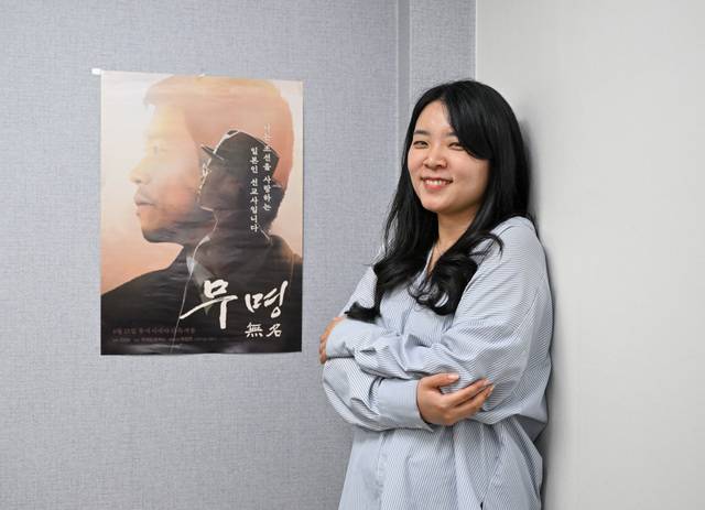 유진주 감독이 지난 18일 서울 용산구 CGN 본사에서 다큐멘터리 ‘무명(無名)’ 포스터 앞에 서서 환하게 웃고 있다. 영화는 25일 개봉한다. 신석현 포토그래퍼