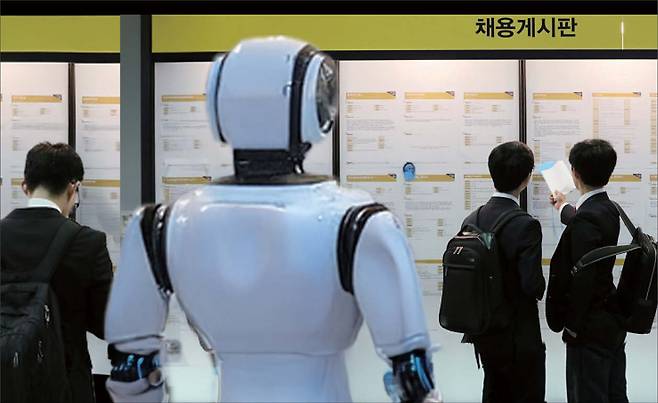 인공지능(AI)발 인력 구조 변화 여파가 신입 채용 한파로 이어지고 있다. 챗GPT 등의 AI가 IT 직군 등의 기본 업무를 빠르게 대체하고 있기 때문이다. 사진은 최근 열린 한 취업 박람회. 고용정보 게시판을 살펴보고 있는 취업준비생들 뒤로 현장에 전시된 AI 로봇의 뒷모습이 보인다.   [헤럴드DB]