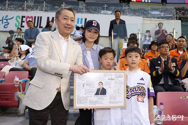 두산 구단주인 박정원 두산그룹 회장(왼쪽)이 24일 잠실구장에서 열린 ‘소방가족 마음돌봄’ 행사에서 2018년 순직한 심문규 소방장의 유가족에게 AI로 복원한 가족사진을 선물한 뒤, 쌍둥이 자녀로부터 롤링페이퍼를 선물받았다. 사진제공｜두산 베어스