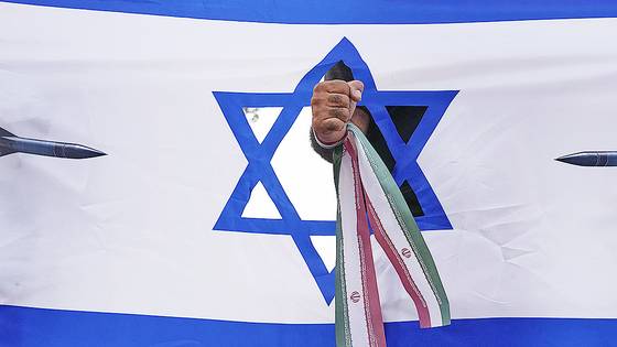 24일(현지시간) 이란 수도 테헤란에서 한 시민이 이스라엘의 자국 영토 공격에 항의하기 위해 이란 국기로 손목을 묶은 뒤 주먹으로 이스라엘 국기를 뚫는 퍼포먼스를 하고 있다. AP=연합뉴스