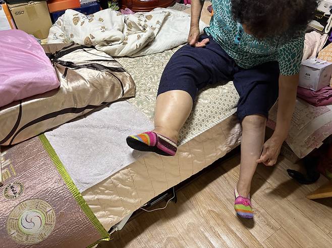 김모(여·84) 씨가 약 2평 남짓한 방 침대에 앉아 부어오른 다리를 설명하고 있다. 사진=김세영 기자
