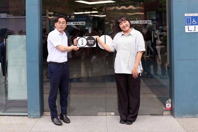 이원주 산업통상자원부 대변인과 에너지 절약 공익 광고 모델인 개그우먼 이수지씨가 2일 서울 중구 인근에서 온도주의 캠페인에 참여 중인 매장을 찾아 여름철 에너지 절약 스티커를 출입문에 붙이고 있다. 산업통상자원부 제공