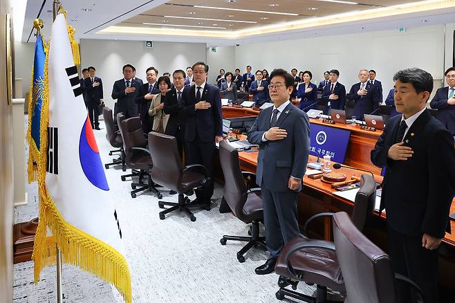 President Lee Jae Myung, center, and ministers show respect for the flag ahead of a Cabinet meeting at the presidential office in Yongsan District, central Seoul, on June 24. [JOINT PRESS CORPS]