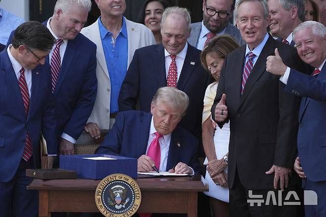 [워싱턴=AP/뉴시스]도널드 트럼프 미 대통령이 4일(현지시각) 백악관에서 의원들에게 둘러싸인 채  감세 및 지출 을 규정하는 메가법안에 서명하고 있다. 2025.7.5.