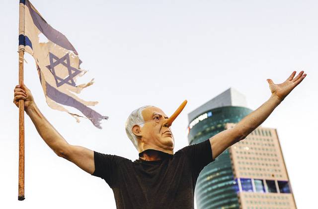 이스라엘 텔아비브 국방부 청사 앞에서 5일(현지시간) 하마스에 억류된 인질들의 석방을 촉구하는 집회 참가자가 베냐민 네타냐후 총리 얼굴에 피노키오 코를 붙인 가면을 쓰고 찢어진 국기를 들고 있다. AFP연합뉴스