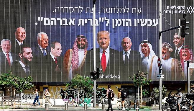 이스라엘 광고판에 트럼프 등장 이스라엘 텔아비브의 한 건물에 26일(현지시간) ‘지금은 아브라함 협정의 시간’이라는 히브리어 문구가 적힌 광고판이 걸려 있다. 아브라함 협정은 이스라엘과 일부 아랍 국가가 외교 관계를 수립한 협정이다. 광고판에는 도널드 트럼프 미국 대통령과 무함마드 빈살만 사우디아라비아 왕세자(왼쪽 여섯 번째), 베냐민 네타냐후 이스라엘 총리(여덟 번째) 등의 얼굴이 그려져 있다. AFP연합뉴스