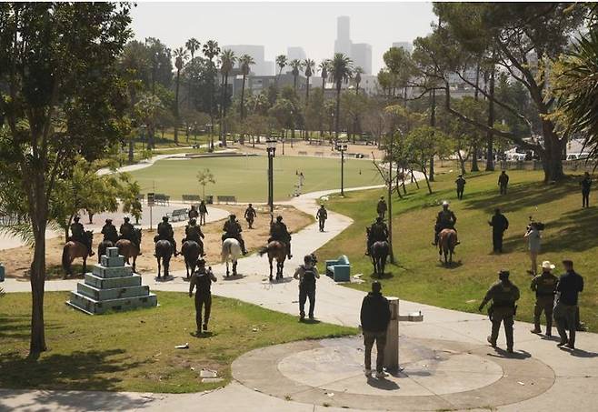 [로스앤젤레스=AP/뉴시스] 7일 로스앤젤레스 맥아더 공원에서 연방 요원들이 말을 타고 불법 이민자를 찾고 있다. 제복에 ‘경찰 미국 국경 순찰대’와 ‘국토안보수사국’의 약자인 ‘HSI’가 적혀 있다. 2025.07.08. *재판매 및 DB 금지
