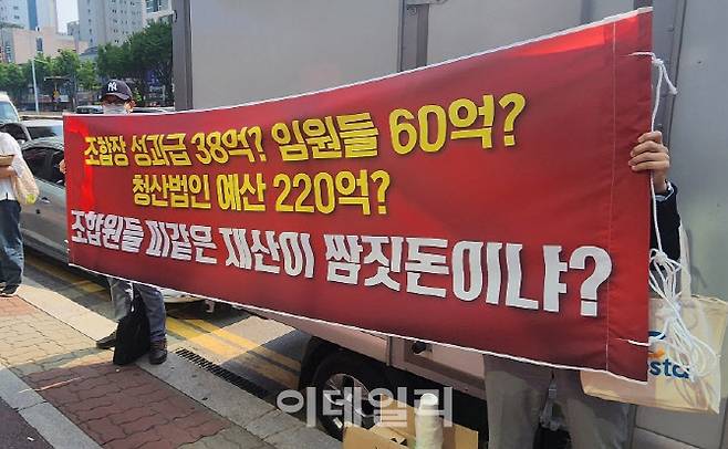 평촌 어바인스트 조합원들이 조합장과 임원들 성과급 지급을 반대하는 현수막을 들고 시위하고 있다.(사진=제보자)