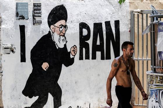 이스라엘 정부가 자국과 미국의 지난달 이란 핵시설 공격 이후에도 이란이 핵무기 원료가 될 수 있는 농축우라늄 비축분 일부를 여전히 보유하고 있다는 결론을 내렸다. 8일 이스라엘 텔아비브에서 한 남성이 이란 최고 지도자 아야톨라 알리 하메네이의 그림이 그려진 벽 옆을 걷고 있다. 로이터=연합뉴스