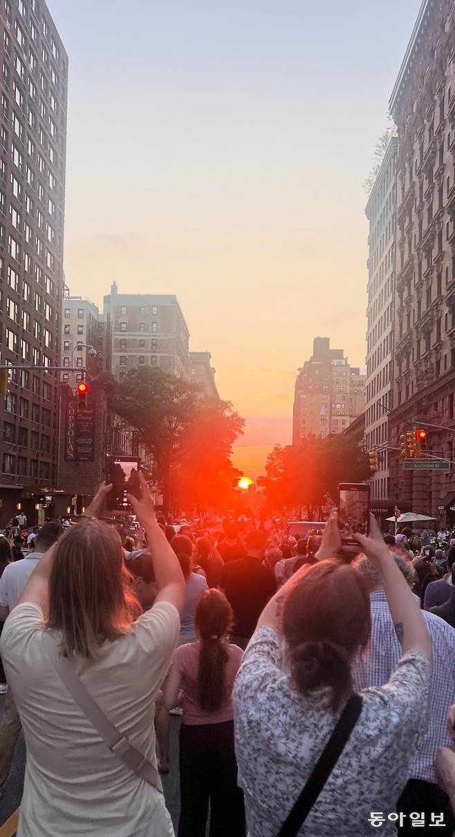 11일 오후 미국 뉴욕 맨해튼 79번가 고층 건물 사이 도로와 석양이 가깝게 겹치는 이른바 ‘맨해튼헨지’ 현상이 나타나자 시민들이 발걸음을 멈춘 채 일제히 휴대전화로 사진을 찍고 있다. 뉴욕=임우선 특파원 imsun@donga.com