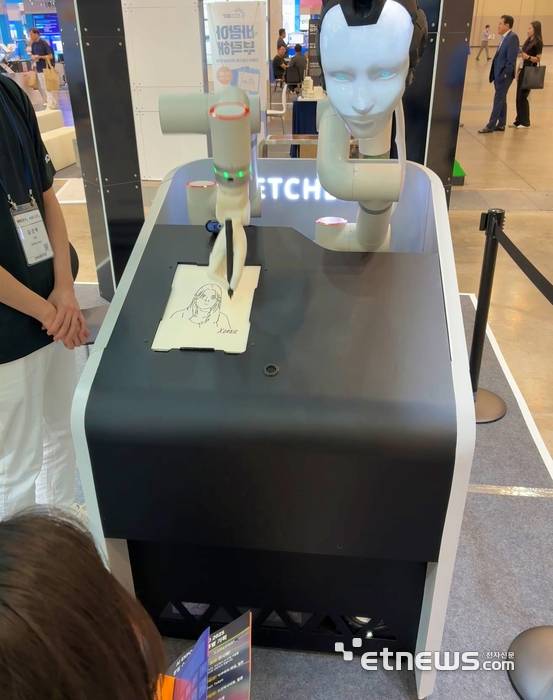 엑스오비스 부스에서 로봇이 관람객 얼굴을 만화가 이현세 스타일로 그리고 있다.