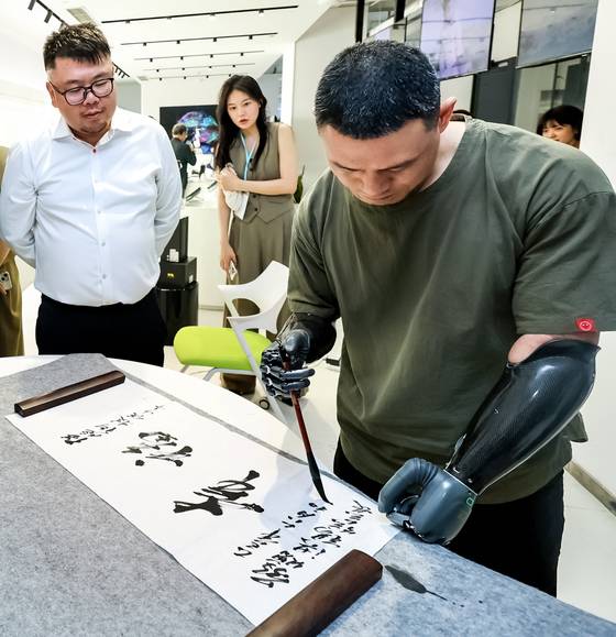 양손을 잃고 브레인코의 스마트 인공 손을 착용한 남성이 한비청 CEO 옆에서 붓글씨를 쓰고 있다. 장진영 기자