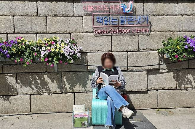A visitor reads at the Seoul Outdoor Library, a public reading space set up along Cheonggyecheon in central Seoul. Its summer season ran from April 23 to June 29, with a fall session scheduled to begin in September. (Seoul Metropolitan Government)