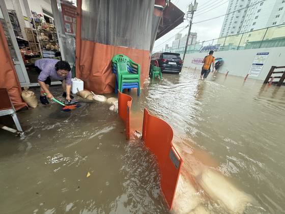A shop owner sweeps out rainwater from a flooded store in Baegun-dong, Nam District, Gwangju, on July 17, as a heavy rain warning went into effect. [NEWS1]