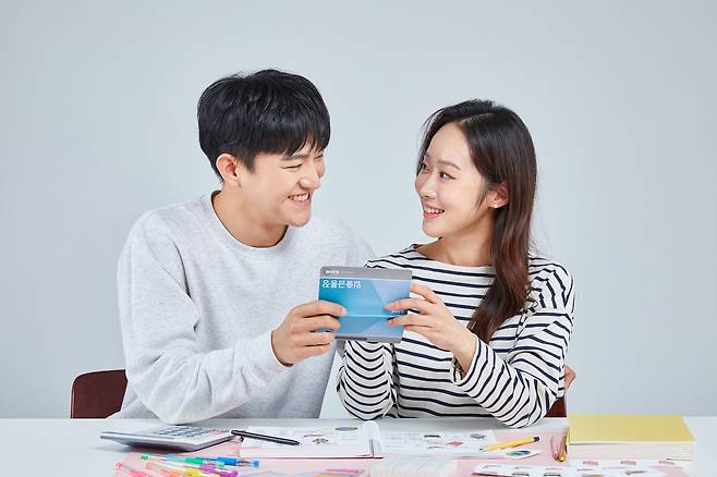 A young couple smiles while holding a shared bank passbook. [GETTY IMAGES BANK]