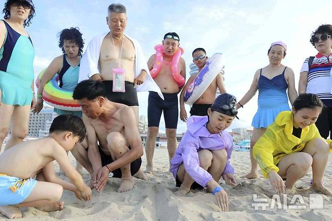 [원산=AP/뉴시스] 지난 2일 북한 강원도 원산의 원산-갈마 해안관광지구에서 어린이들이 모래사장에 '우리 조국'이라고 쓰는 모습을 어른들이 지켜보고 있다. 북한 노동신문은 갈마관광지구 개장 소식을 알리며 "세상에 없는 황홀한 관광 명소"라고 선전했다. 원산 명사십리 해변 일대에 지어진 관광지구 개발은 북한이 11년간 공들인 숙원사업으로 알려져 있다. 2025.07.18.