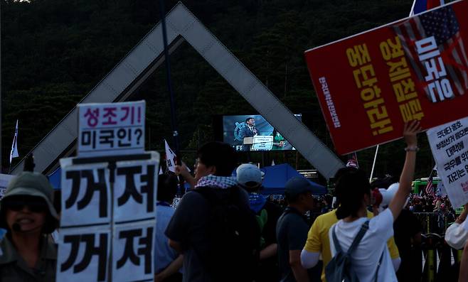 ‘사기꾼 모스 탄 방한 반대 대학생 긴급행동’이 2025년 7월15일 저녁 서울 관악구 서울대 정문 안에서 규탄 기자회견을 하고 있다. 정문 너머로 탄 교수가 발언하는 영상이 전광판에 비치고 있다.