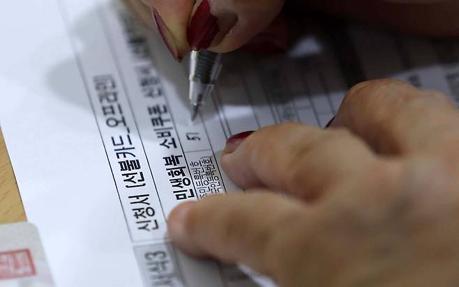 한 시민이 21일 서울 동대문구 용두동 주민센터에서 민생회복 소비쿠폰 카드를 발급받기 위해 신청서를 작성하고 있다. 허정호 선임기자