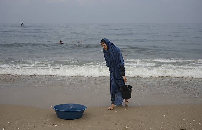 한 팔레스타인 여성이 가자지구 해변에서 옷을 빨기 위해 바닷물을 모으고 있다. AP연합뉴스