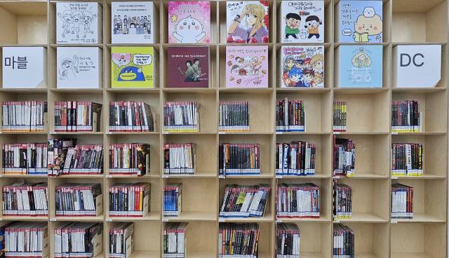 만화 라운지 책장에 꽂힌 마블·DC 코믹스 만화책들. 상단에 있는 유명 웹툰 작가들의 축전도 눈길이 간다.