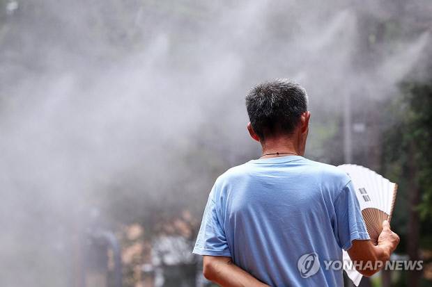 서울 한낮 기온이 34도까지 치솟으며 무더운 날씨를 보인 지난 24일 서울역 쪽방촌 인근 한 공원에서 주민이 쿨링포그를 맞으며 부채질을 하고 있다. 연합뉴스