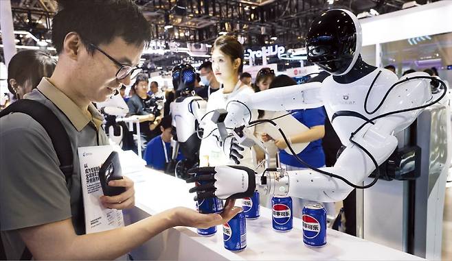 < 음료수 건네는 휴머노이드 > 지난 26일 중국 상하이에서 열린 ‘2025 세계인공지능대회(WAIC)’에 휴머노이드 로봇 약 60종이 전시된 가운데 중국 로봇 스타트업 애지봇 부스에서 휴머노이드 로봇이 관람객에게 탄산음료를 건네주고 있다.  로이터연합뉴스