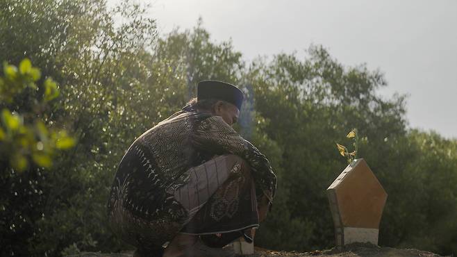 인도네시아 자와 틍아주 데막군 한 해안가 마을에 거주하는 65세 어부 무하마드 루시판 씨가 아내의 무덤 앞에 앉아 있다.[그린피스 제공]