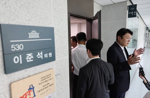 개혁신당 김정철 최고위원이 30일 서울 여의도 국회 의원회관 이준석 의원실 앞에서 ‘김건희특검 관련 압수수색 절차적 문제점 및 준항고 주요 이유 언론 브리핑’을 하고 있는 가운데 특검 관계자들이 압수수색을 위해 의원실로 들어가고 있다. [연합뉴스]