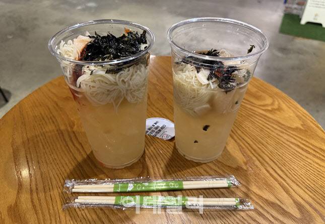 CGV ‘컵냉면’ 실물 구성. 투명 컵에 면과 고명이 층층이 담겨 있으며, 함께 제공된 나무젓가락 두 개가 테이블 위에 놓여 있다. 비주얼만큼은 꽤 그럴싸하다. (사진=한전진 기자)
