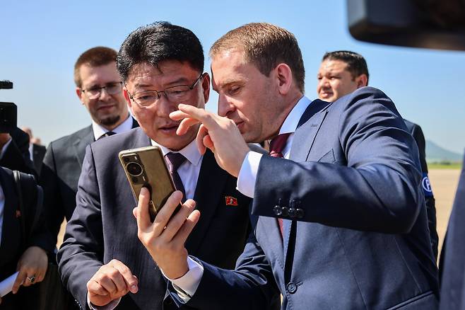 North Korean External Economic Relations Minister Yun Jong-ho, left, and Russian Natural Resources Minister Alexander Kozlov look at a phone together following a ceremony at Pyongyang International Airport on July 28 marking the arrival of the first direct flight from Moscow to the North Korean capital in decades. [AP/YONHAP]