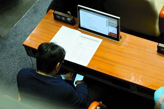 Rep. Lee Choon-suak of the Democratic Party, who chairs the National Assembly’s Legislation and Judiciary Committee, appears to check a trading account registered to another person’s name during a plenary session at the National Assembly in Yeouido, western Seoul, on Aug. 4. [THE FACT]