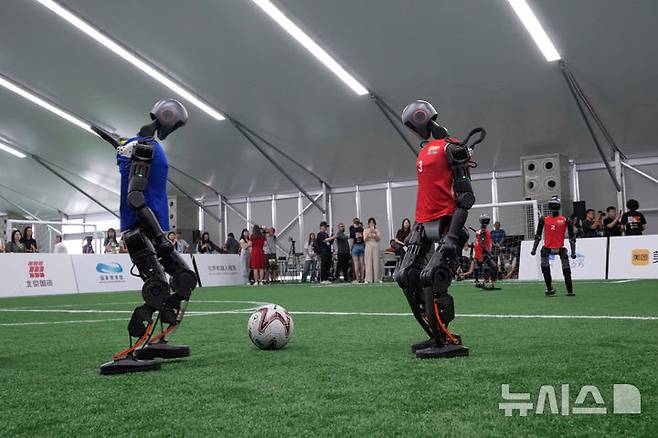 [베이징=AP/뉴시스] 4일(현지 시간) 중국 베이징에서 '2025 세계 휴머노이드 로봇 게임'을 앞두고 언론 공개 행사가 열린 가운데 부스터 휴머노이드 로봇들이 축구 시범 경기로 기술을 선보이고 있다. 오는 14일부터 17일까지 열리는 이 행사에는 축구를 비롯해 달리기, 격투, 댄스 등 실제 사람의 경기와 유사한 종목이 포함된 것으로 알려졌다. 2025.08.04.