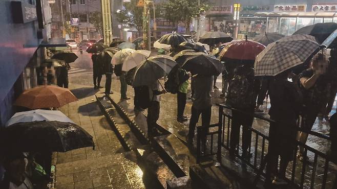 비 오는 새벽, 서울 구로구 남구로역 사거리. 일용직 노동자들이 빗속에서 우산을 든 채 일자리를 기다리고 있다.[사진 | 더스쿠프 포토]