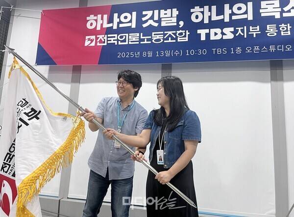▲13일 서울 마포구 상암동 TBS 사옥 1층 오픈스튜디오에서 TBS노동조합과 전국언론노동조합 TBS지부의 통합 선포식이 열렸다. 이정환·송지연 언론노조 TBS지부 공동비대위원장이 함께 깃발을 흔들고 있다. 사진=정민경 기자.