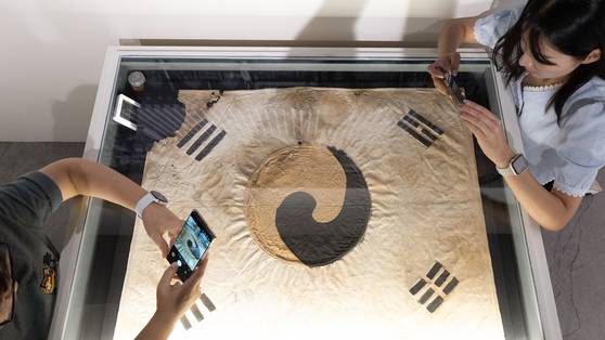 Visitors take pictures of the historic Taegeukgi from Jingwan Temple in Seoul at Korea Heritage Service's exhibition titled “The Radiant Heritage of Independence” at Deoksu Palace in Jongno District, central Seoul, on Monday. [JOONGANG ILBO]