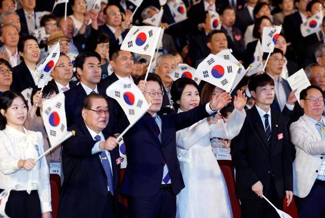 이재명 대통령과 김혜경 여사가 15일 서울 종로구 세종문화회관에서 열린 제80주년 광복절 경축식에서 참석자들과 태극기를 흔들고 있다. 뉴시스