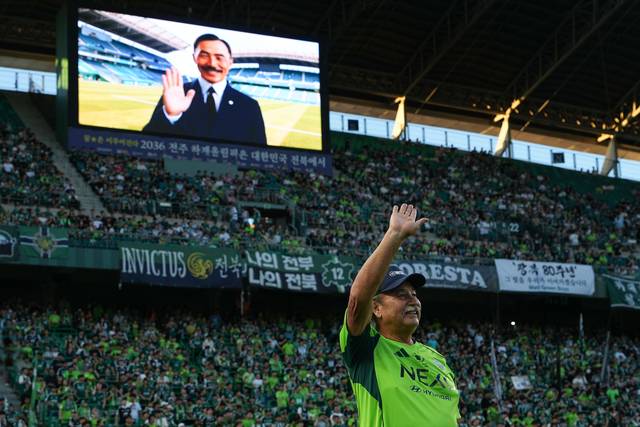 도산 안창호 선생의 외손자인 필립 안 커디씨가 16일 전주월드컵경기장에서 팬들에게 인사하고 있다. 필립 안 커디씨 뒤쪽으로는 AI로 복원된 도산 안창호 선생이 미소를 짓고 있다. [전북현대 제공]