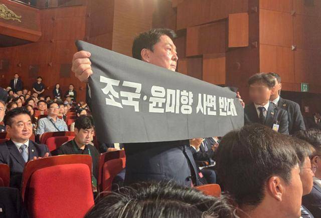 안철수 국민의힘 당대표 후보가 15일 서울 종로구 세종문화회관에서 열린 제80주년 광복절 경축식에 참석해 경축사 중인 이재명 대통령을 향해 조국 전 조국혁신당 대표와 윤미향 전 의원의 사면 반대 플래카드를 들어보이며 항의하고 있다. 안철수 캠프 제공