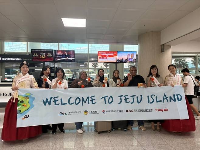 “웰컴 투 제주”. 한복을 입은 도우미들과 싱가포르 관광객들이 제주 입도 환영 배너 앞에서 기념 촬영을 하고 있다. (제주관광공사 제공)