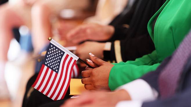 미국 귀화식에서 성조기를 들고 앉아있다. (사진=게티이미지)