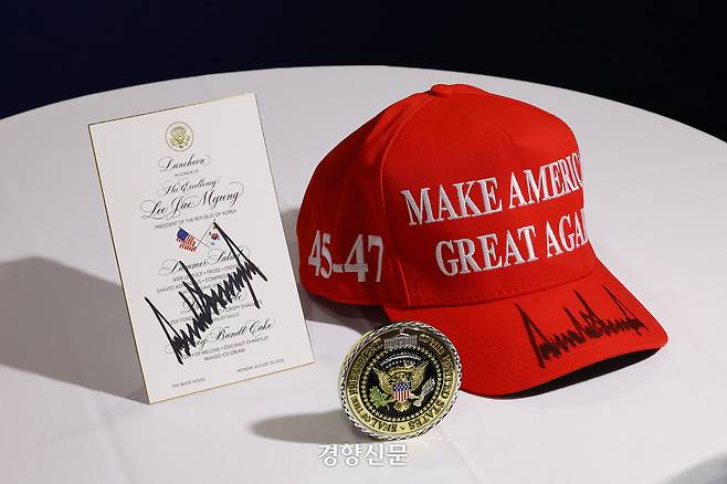 이재명 대통령이 트럼프 미국 대통령으로부터 받은 선물.  트럼프 대통령이 서명해준 오찬 메뉴판,  마가(MAGA·Make America Great Again) 모자,  백악관 기념 메달(Presidential Challenge Coin). 김창길 기자