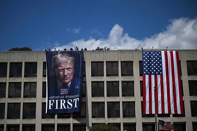 Workers hang a large photo of U.S. President Donald Trump next to a U.S. flag on the facade of the Department of Labor headquarters building in Washington on Aug. 27. [AFP/YONHAP]